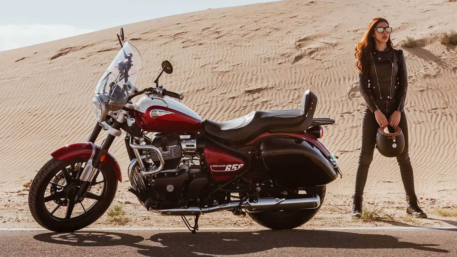 A biker standing with a Celestial Red Royal Enfield Super Meteor 650 in a desert